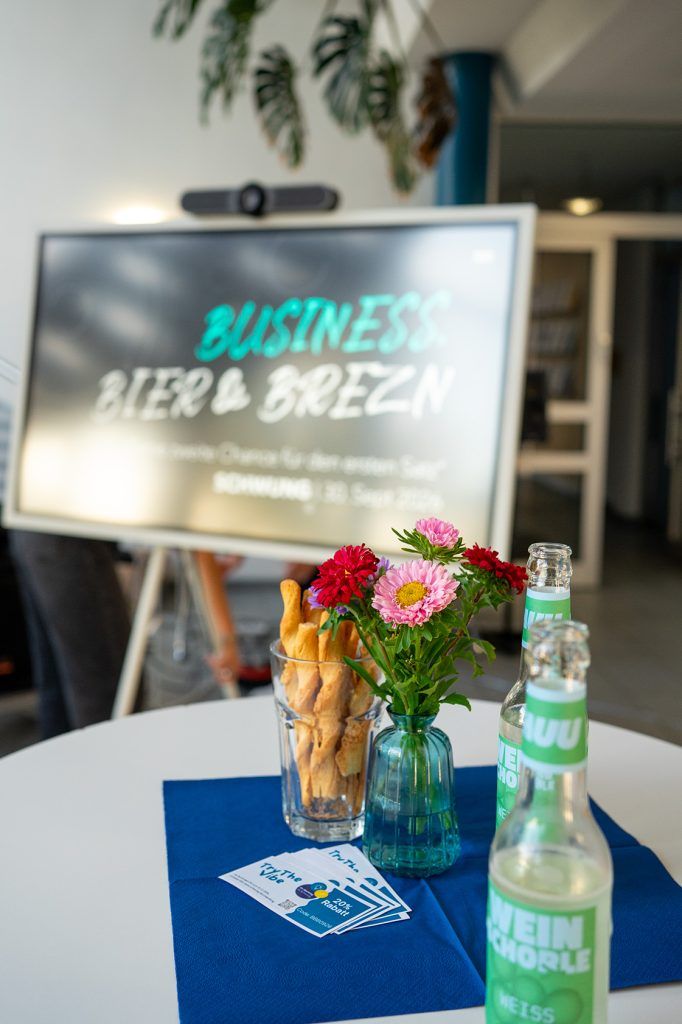 Begrüßungsschild „Business, Bier & Brezn“ mit Blumen am Eingang